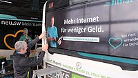 Ein Mann auf einer Leiter beklebt einen Bus mit Werbung für fitfalt. 