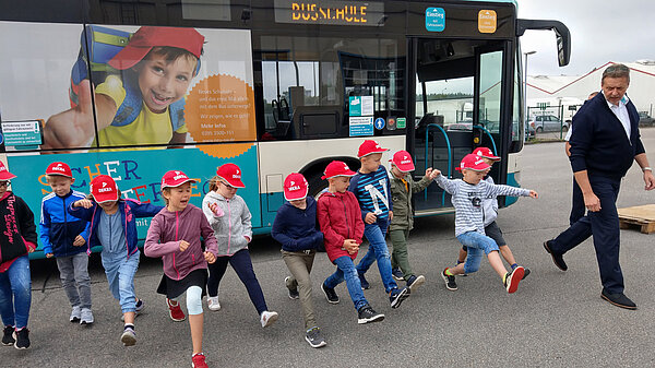 Kinder mit Busfahrer vor einem Stadtbus.