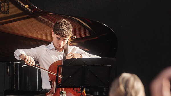Junger Musiker mit Cello vor Klavier.