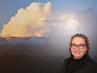 Eine Frau mit Brille vor einem Wolkenbild