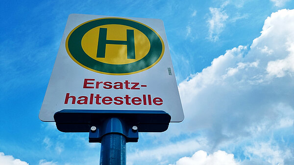 Haltestellenschild mit grünem H in gelbem Kreis. Darunter in roter Schrift "Ersatzhaltestelle". 