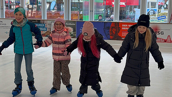 vier Mädchen Hand in Hand auf dem Eis.