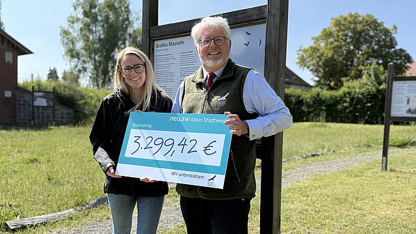 Vertreterin von neu.sw und Vertreter der Deutschen Wildtier Stiftung halten den großen sympolischen Scheck, auf dem die Spendensumme in Höhe von 3299,42 Euro notiert ist.