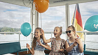 Drei Kinder mit blauen und orangen Luftballons im neu.sw Linienschiff.