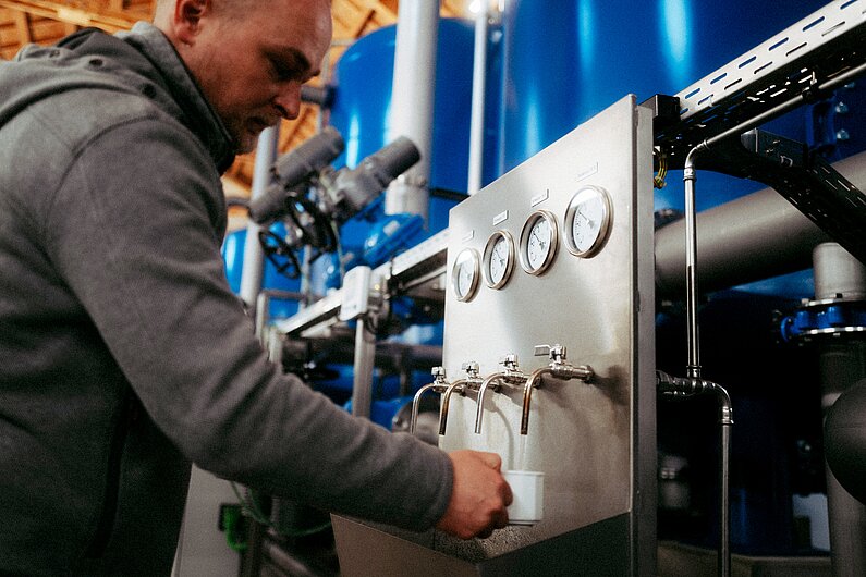Mitarbeiter im Wasserwerk entnimmt Wasser aus einem Hahn.