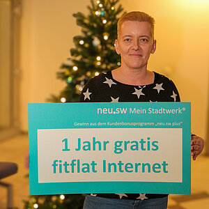 Frau vor Weihnachstbaum mit Gewinn fitfalt.