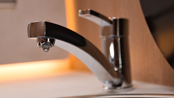 Silbener Wasserhahn mit Wassertropfen.