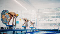 Sportler stehen in vorgebeugter Starthaltung auf Startblöcken in der neu.sw Schwimmhalle. 