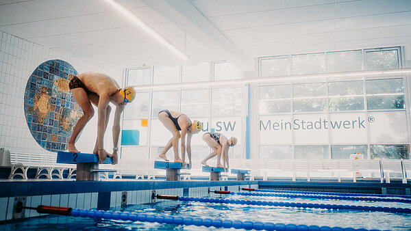 Drei Schwimmer in Startposition auf Startblöcken in der neu.sw Schwimmhalle.