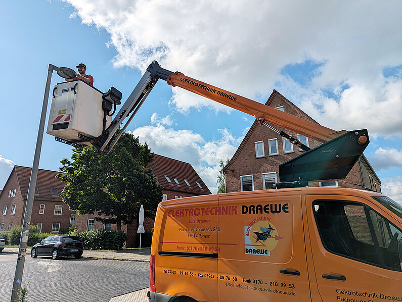 Mitarbeiter in einem Arbeitskorb arbeitet an Leuchte einer Straßenlaterne.  