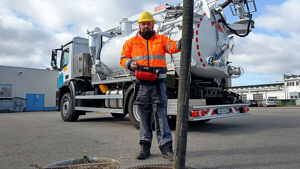 Arbeiter in Warnweste vor Saugwagen.