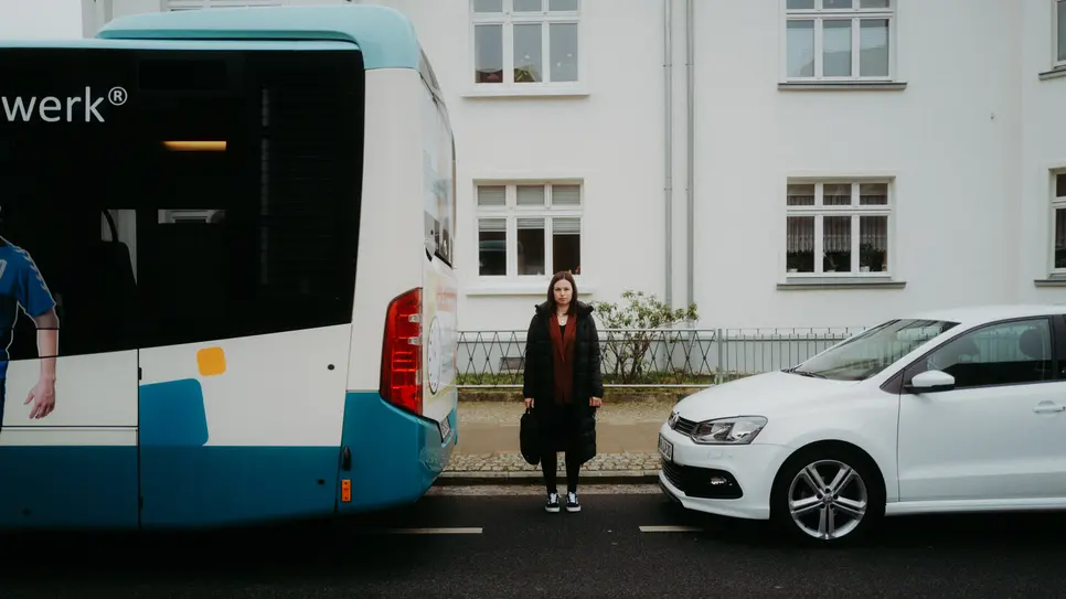 Eine junge Frau steht zwischen einem Bus und einem Auto 