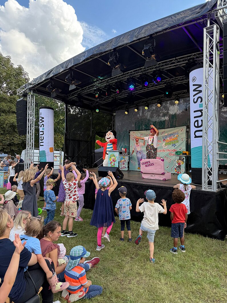 Kinder vor einer Bühne verfolgen das Programm eines Clowns.