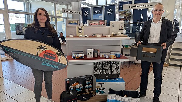 Geschäftsführer Peter Kuboth und Mitarbeiterin Yasemin Deveci mit Artiekln aus dem VW- und Skoda-Shop. Sie halten einen Feuerholz-Kasten und ein kleines Surfbrett in den Händen.