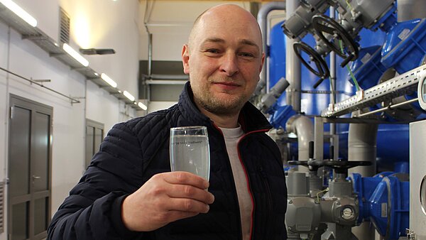 Mitarbeiter imm Wasserwerk hält gefülltes Wasserglas in die Kamera.