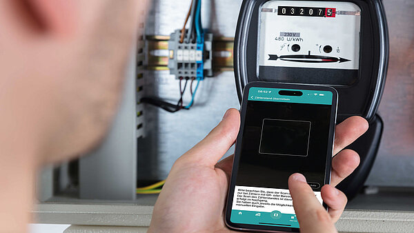 Mann überträgt per Smartphone die Angaben auf einem Strom- bzw. Gaszähler.