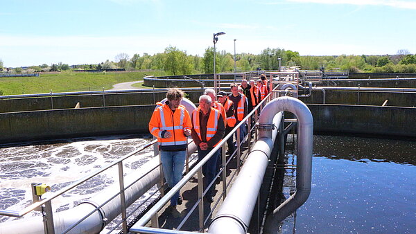 Gruppe in orange-farbenen Warnwesten beim Gang auf der Brücke eines Rundbeckens.