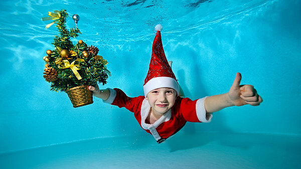 Kind im Weihnachtsmannkostüm taucht unter Wasser im Schwimmbecken.