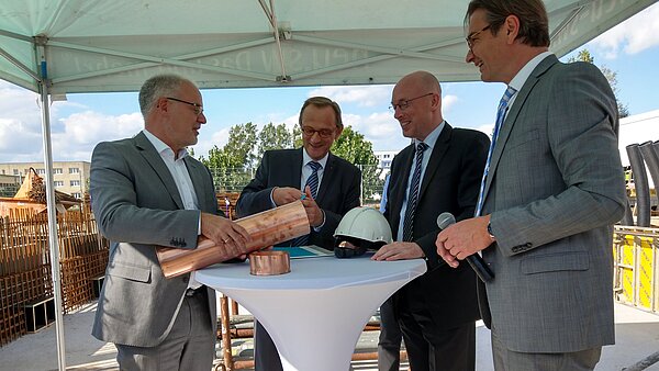 Vize-Oberbürgermeister Peter Modemann, der erste Stellvertreter des Landrats Kai Seiferth, Energieminister Christian Pegel und neu.sw Geschäftsführer Ingo Meyer (v.l.n.r.) stehen an einem weißen runden Tisch und füllen die Zeitkapsel.