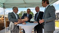 Vize-Oberbürgermeister Peter Modemann, der erste Stellvertreter des Landrats Kai Seiferth, Energieminister Christian Pegel und neu.sw Geschäftsführer Ingo Meyer (v.l.n.r.) stehen an einem weißen runden Tisch und füllen die Zeitkapsel.