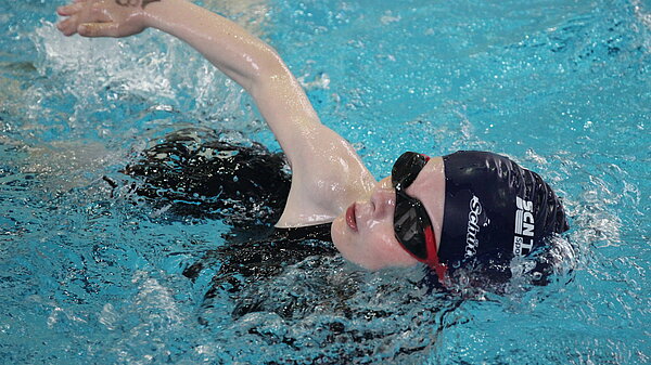 Kinder krault mit Badekappe und Schwimmbrille im Schwimmbecken.