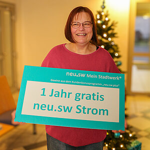 Frau im roten Poullover mit Gewinnscheck vor einem Weihnachtsbaum