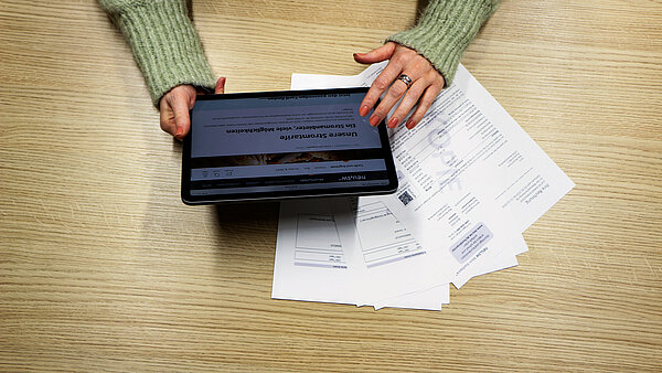 Frauenhände halten ein Tablet über einer Papier-Abrechnung.