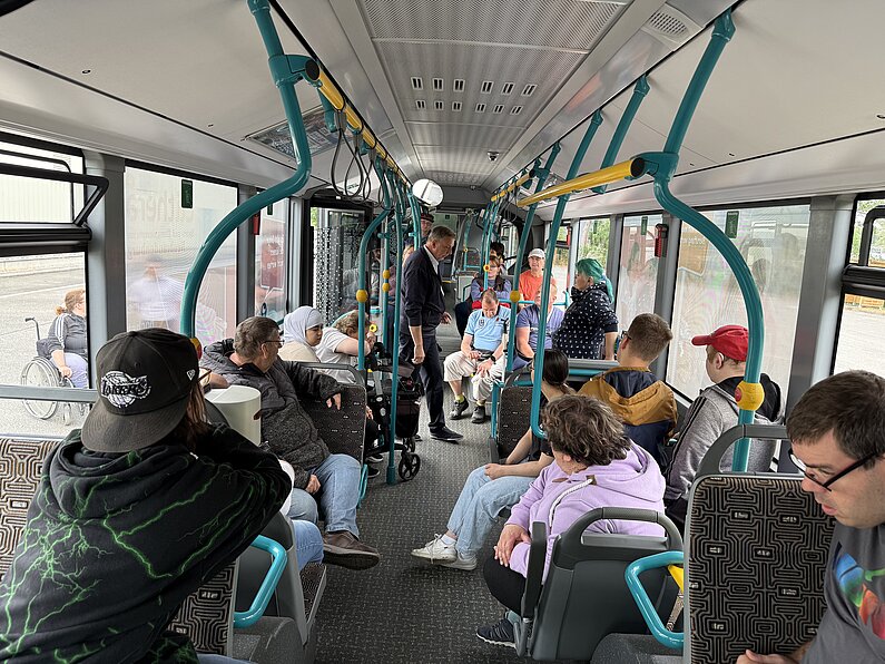 Teilnehmende sitzen im Stadtbus und hören Erklärungen eines Busfahrers.
