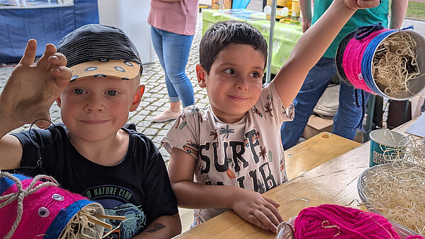 Zwei kleine Jungen mit selbst gebastelten bunten Bienenhotels aus Blechbüchsen.