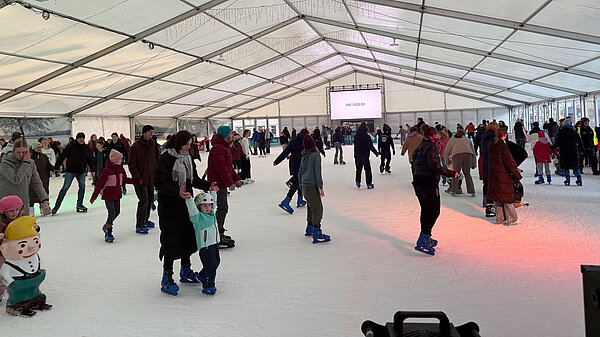 Blick in die volle Eislaufhalle mit vielen Menschen auf dem Eis.