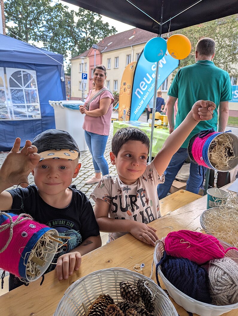 Zwei kleine Jungen mit selbst gebastelten bunten Bienenhotels aus Blechbüchsen.