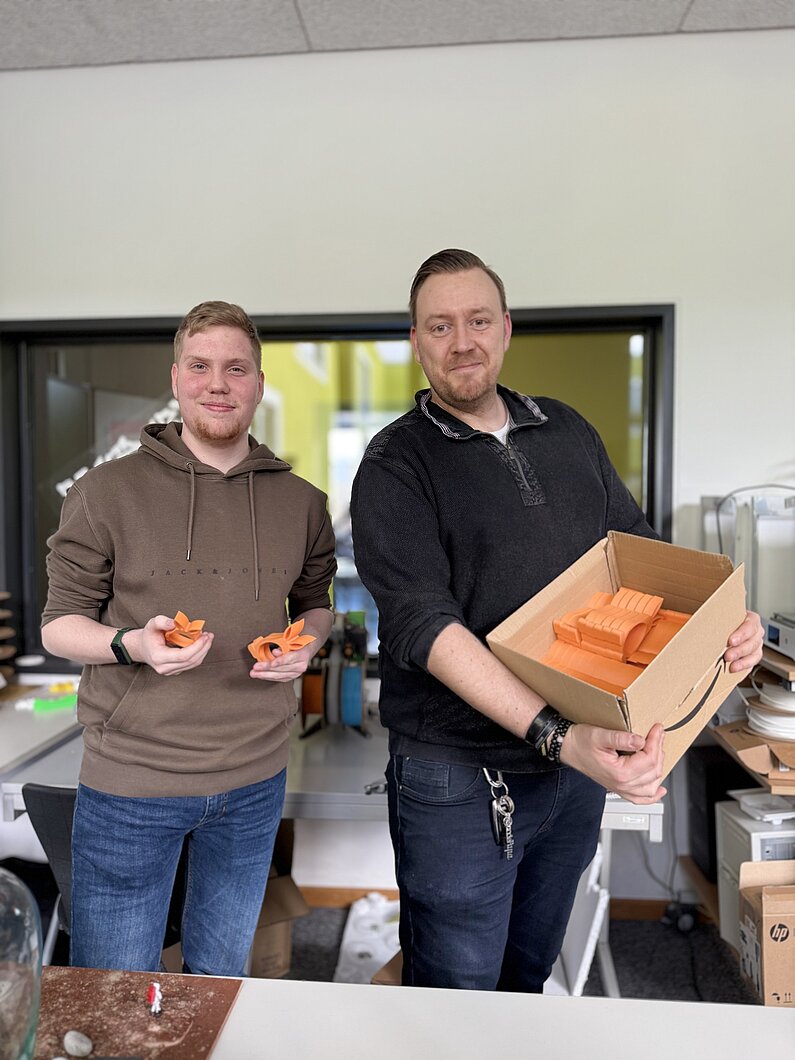 Lehrer und Schüler präsentieren fertige orangefarbene Osterhasen in einem Karton.