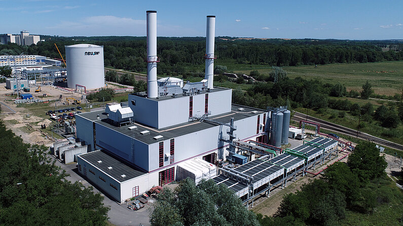 Blick auf das GuD-Heizkraftwerk mit seinen zwei langen Schornsteinen. Im Hintergrund der zylinderförmige weiße Kurzzeitwärmespeicher.
