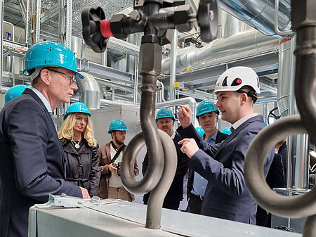 Zwei Männer mit Arbeitsschutzhelmen unterhalten sich in einer Industrieanlage.