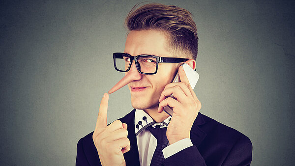 Junger Mann mit langer Lügennase telefoniert mit Handy.