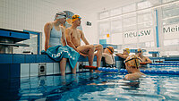 Jugendliche Badegäste am Beckenrand und im Wasser der neu.sw Schwimmhalle. 