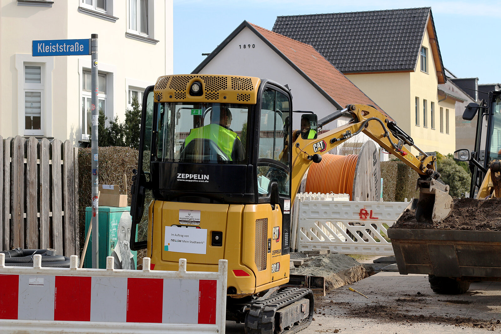 Bagger vor Kabeltrommel schaufelt Erde aus Graben.