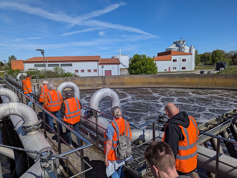 Gruppe in orange-farbenen Westen bei Führung über Kläranlage. Hier die CAST-Becken zur biologischen Abwasser-Reinigung.