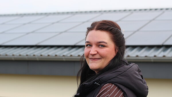 Das Foto zeigt Mareike Poley vor einer PV‑Dachanlage – ein Hintergrund, der für viele ihrer Arbeitsaufgaben steht, die sie normalerweise vom Schreibtisch aus begleitet. 