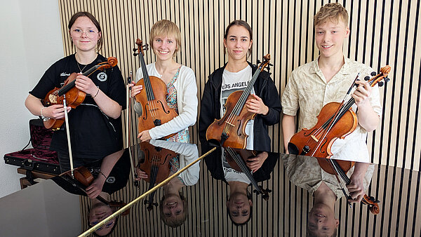 Ella Vöske, Merle C. Döhnert, Mathea Weimann und Jakob Rau stehen mit ihren Bratschen lächelnd hinter einem schwarzen Flügel. 