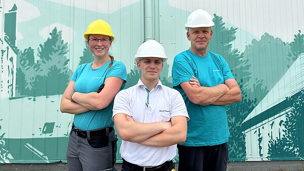 Gruppenbild: Eine Mitarbeiterin und ein Mitarbeiter in neu.sw Shirts lächenld mit verschränkten Armen vor einem neu.sw Wandbild.