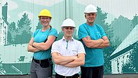 Drei lächelnde Stadtwerke-Mitarbeiter mit verschränkten Armen vor einem Stadtwerke-Wandbild.