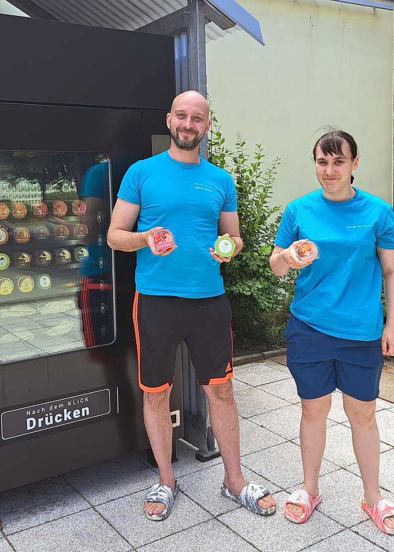 Mitarbeiterin und Mitarbeiter der neu.sw Schwimhalle stehen in neu.sw Shirts mit Eisbechern aus dem Automaten vor dem Automaten.