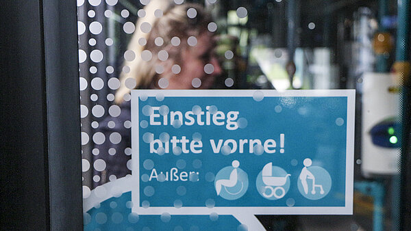 Blaues Hinweisschuld "Einstieg bitte vorne!" im Stadtbus