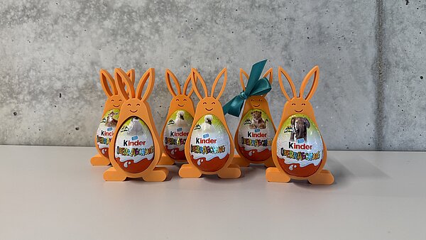 orangefarbene Osterhasen mit Überraschungsei im Bauch, aufgereiht vor grauer Wand.
