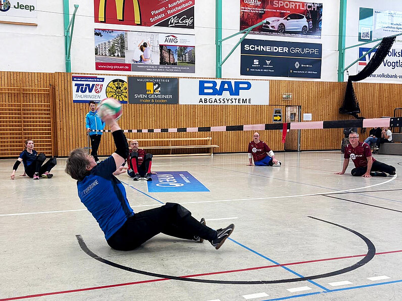 Zwei Mannschften spielen Sitzball in einer Sporthalle. 