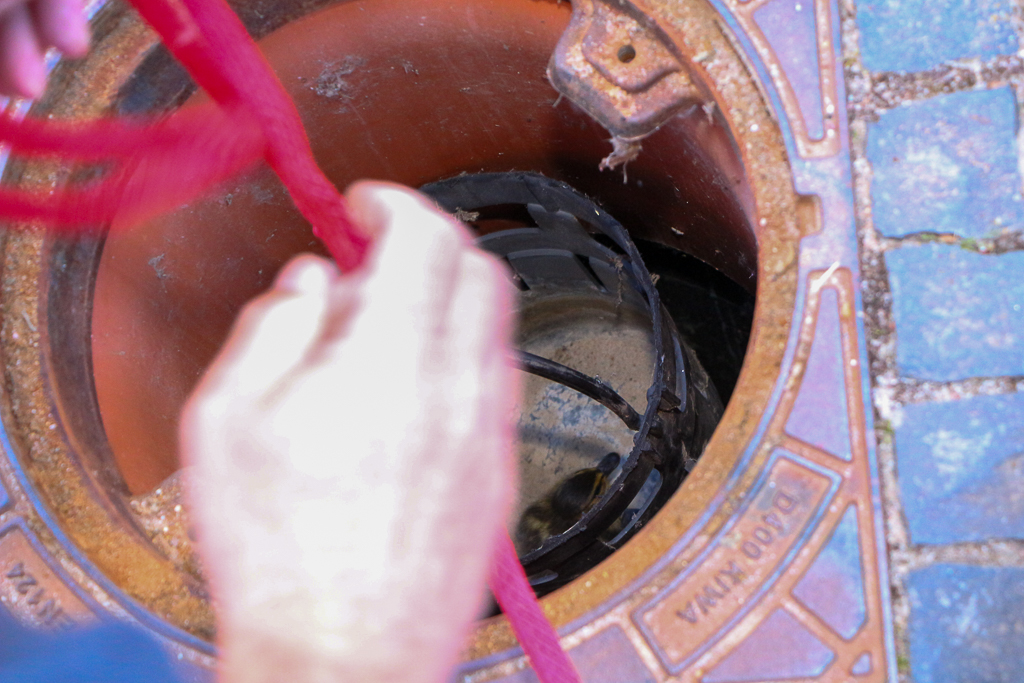 Eine Hand holt einen Behälter mit einem Seil aus einem Schacht.