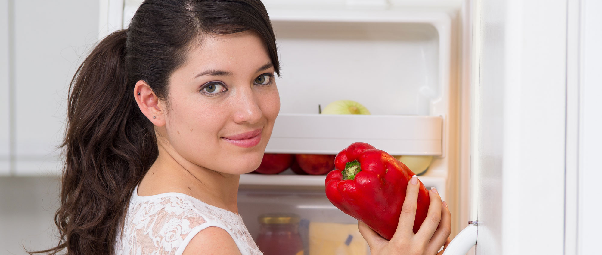 Frau am Kühlschrank mit Paprika in der Hand