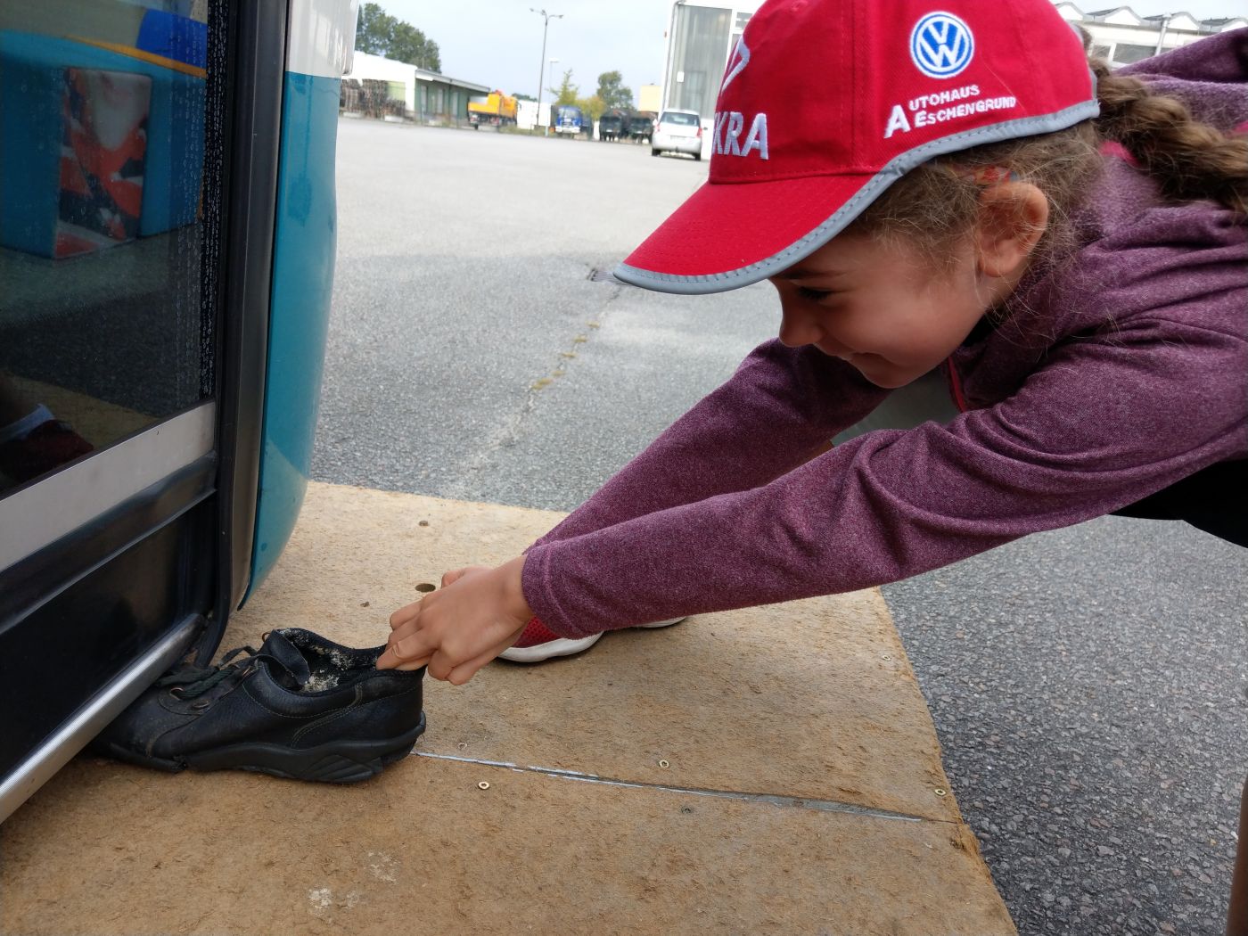 Mädchen beim Versuch, einen eingeklemmten Schuh unter einem Bus hervorzuziehen