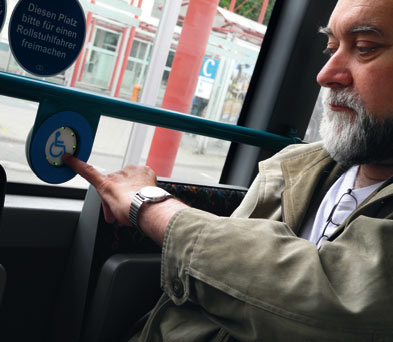Rollstuhlfahrer bedient blauen Taster innerhalb des Busses um seinen Ausstieg mitzuteilen
